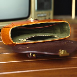 May include: A brown leather handbag with a zippered pocket inside. The bag is open and the lining is green.