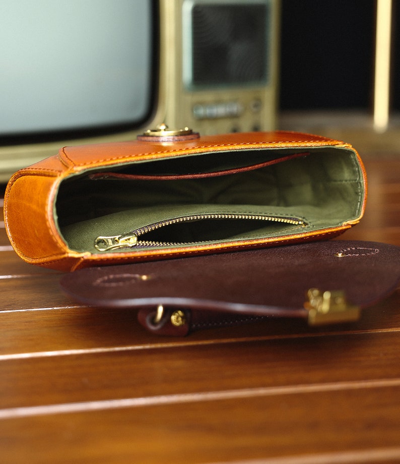 May include: A brown leather handbag with a zippered pocket inside. The bag is open and the lining is green.
