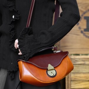 May include: A brown leather satchel bag with a flap closure and a brass lock. The bag has a curved shape and a brown leather strap.