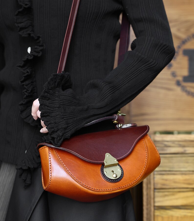 May include: A brown leather satchel bag with a flap closure and a brass lock. The bag has a curved shape and a brown leather strap.