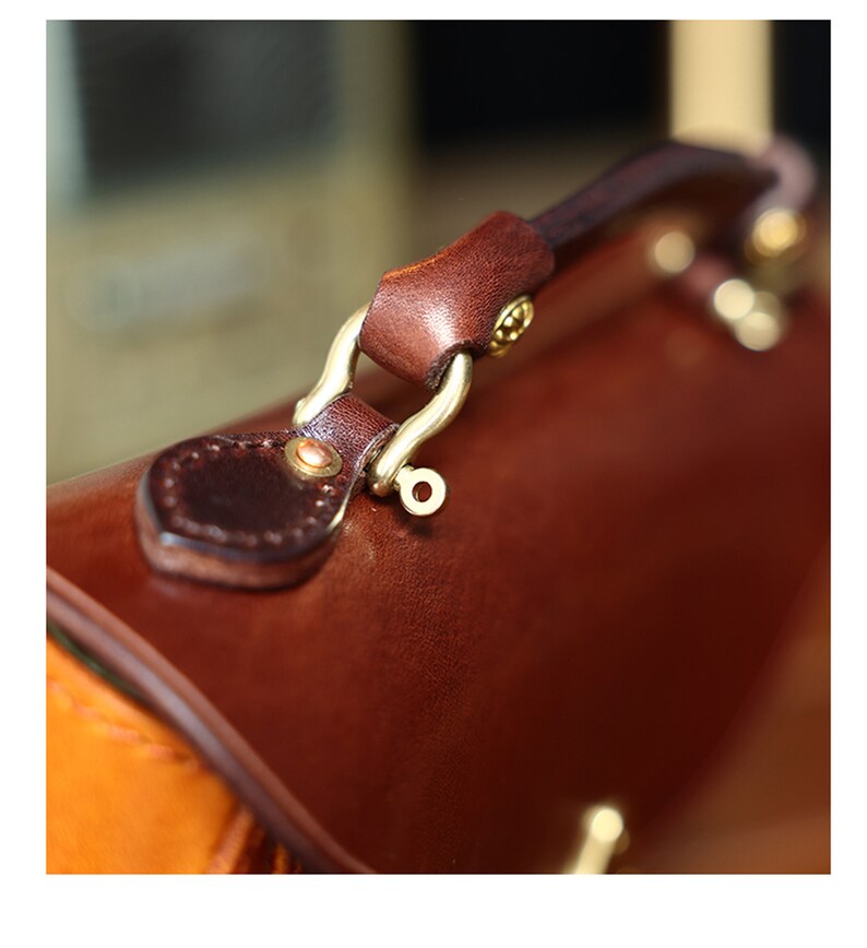 May include: Close-up of a brown leather handbag with a gold metal clasp and handle. The handle is attached to the bag with a decorative metal loop.