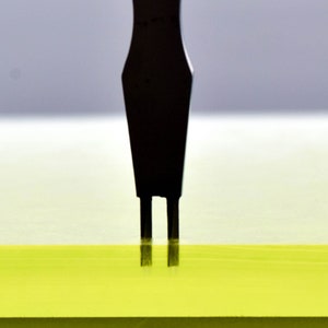 May include: A black tool with two prongs is inserted into a yellow surface.