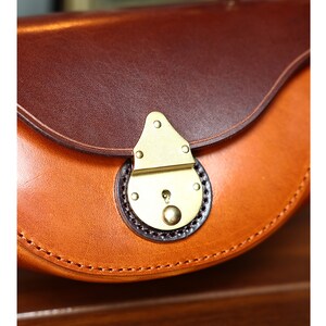 May include: Close-up of a brown leather purse with a brass clasp. The purse has a curved shape and a stitched edge.