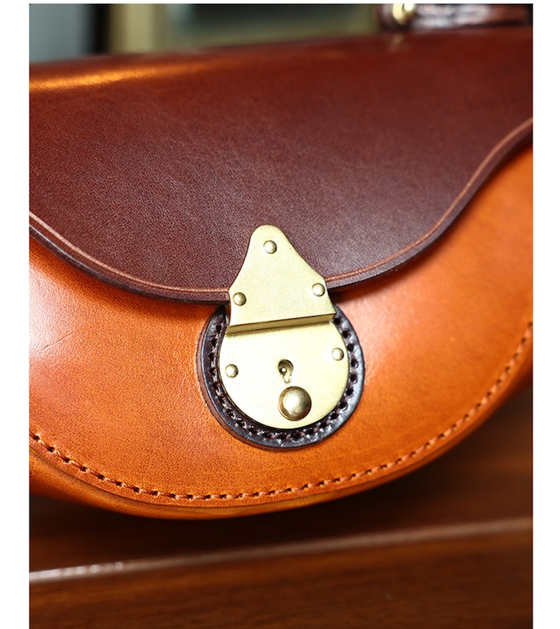 May include: Close-up of a brown leather purse with a brass clasp. The purse has a curved shape and a stitched edge.