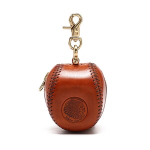 May include: A brown leather baseball-shaped keychain with a gold zipper and a gold clasp. The keychain has a stitched baseball seam design and a Red Moon logo with an American Indian head and the text "Since 1953".