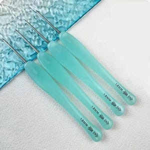 May include: Four metal crochet hooks with light mint green ergonomic handles. Each handle is clearly marked with the text 1.8MM and Chinese characters. The hooks feature a slender silver metal shaft and a pointed tip, designed for fine needlework projects.