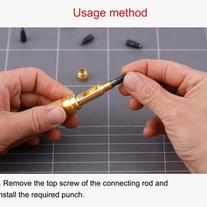 K&ouml;nnte beinhalten: Nahaufnahme einer Hand, die ein Werkzeug aus Messing und Holz mit einem schwarzen Metall-Stempel h&auml;lt. Das Werkzeug dient zum Einsetzen von Nieten. Der Text "Usage method" ist oben im Bild sichtbar. Der Text "1. Remove the top screw of the connecting rod and install the required punch." ist unten im Bild sichtbar.