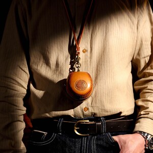 May include: A brown leather pouch with a decorative design hangs from a brown leather cord around a person's neck. The pouch is worn over a striped button-down shirt and blue jeans.