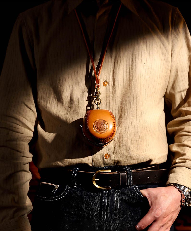 May include: A brown leather pouch with a decorative design hangs from a brown leather cord around a person's neck. The pouch is worn over a striped button-down shirt and blue jeans.