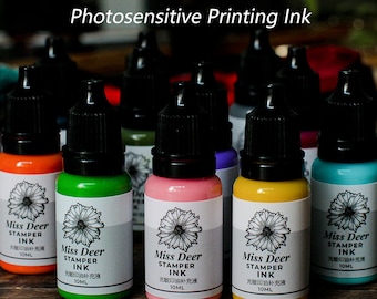May include: Ten bottles of photosensitive printing ink in various colors, including orange, green, pink, yellow, and blue. Each bottle has a black cap and a label with the text "Miss Deer Stamper Ink" and "光敏印油补充液 10ML".