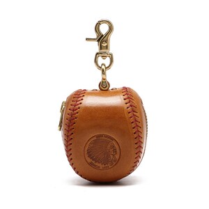May include: A brown leather baseball-shaped coin purse with a red stitching detail and a gold zipper. The purse has a gold metal clasp and a logo that reads "Red Moon Since 1993" with an image of a Native American chief's head.
