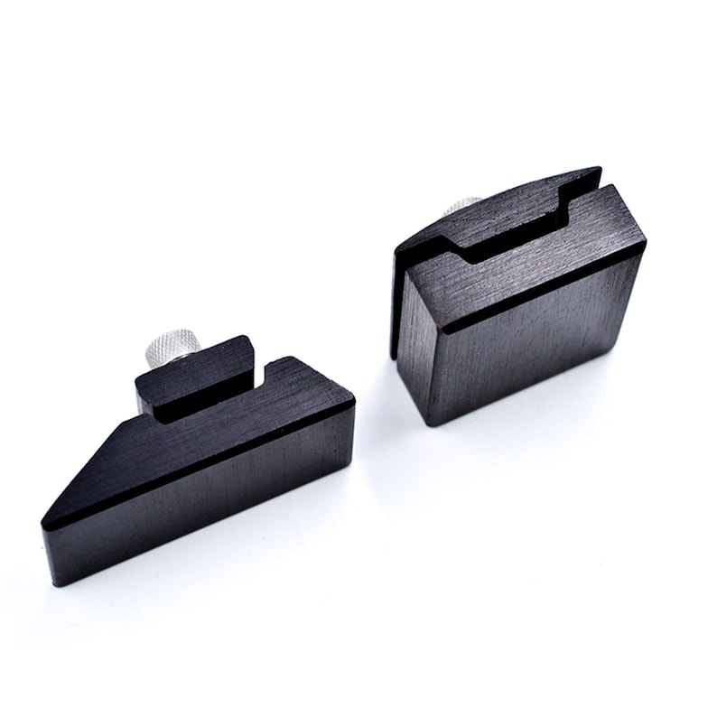 May include: Two black metal clamps with a textured finish. The clamps have a small screw on the top and a slot on the side.