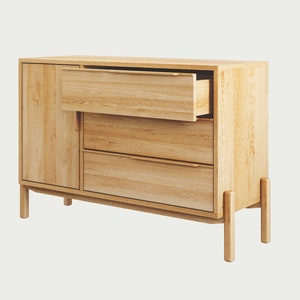 May include: A light wood dresser with three drawers and a cabinet door. The top drawer is open, revealing the wood interior. The dresser has four legs and a simple design.