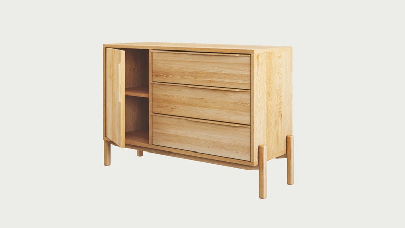 May include: A light wood cabinet with three drawers and a door that opens to reveal a shelf. The cabinet has a modern design with simple lines and a natural finish.