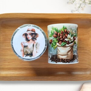 Peut inclure: Deux tasses rondes en céramique à fond blanc et aux motifs colorés. Une tasse représente une femme portant un chapeau tenant une tasse de café. L'autre tasse représente un sac de grains de café avec des fleurs et des feuilles.