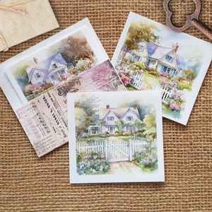 Può includere: Tre acquerelli di case bianche con prati verdi e recinzioni bianche. Le case sono circondate da una vegetazione lussureggiante e fiori. I dipinti sono su cartoncino bianco e sono esposti su uno sfondo di juta.