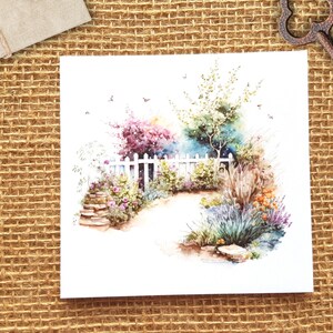 K&ouml;nnte beinhalten: Aquarellmalerei eines wei&szlig;en Lattenzauns mit einem Weg, der durch einen Garten mit Blumen und B&auml;umen f&uuml;hrt. Das Gem&auml;lde hat eine weiche, vertr&auml;umte Atmosph&auml;re.