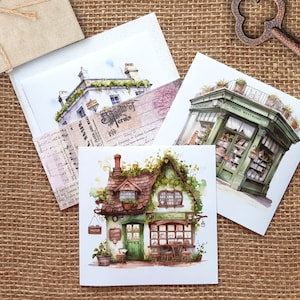 Könnte beinhalten: Drei Aquarell-Illustrationen von Geschäften auf Postkarten. Die erste Postkarte zeigt ein weißes Gebäude mit grünen Ranken und einem Schild mit der Aufschrift "The Spirit of Terms". Die zweite Postkarte zeigt ein grünes Gebäude mit einem Schild mit der Aufschrift "Panic Wentworth". Die dritte Postkarte zeigt ein kleines Häuschen mit einem Schild mit der Aufschrift "The Shop of Curious Things".