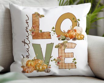 May include: White throw pillow with the word "LOVE" spelled out in large letters. The letters are decorated with fall-themed elements like pumpkins, leaves, and plaid fabric. The text "autumn" is written vertically on the left side of the pillow.