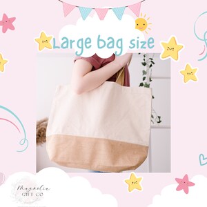 以下が含まれることがあります： 黄色の太陽と星が描かれた白い雲の中に「Large bag size」という文字が書かれた、大きなオフホワイトのキャンバス地のトートバッグ。バッグは人が持っています。バッグの底は茶色のジュート素材です。