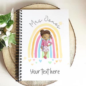 May include: Spiral-bound notebook with a colorful illustration of a person in front of a rainbow. The notebook cover has the text "Mrs Jones" and "Your text here". The person in the illustration is wearing glasses and a pink outfit.