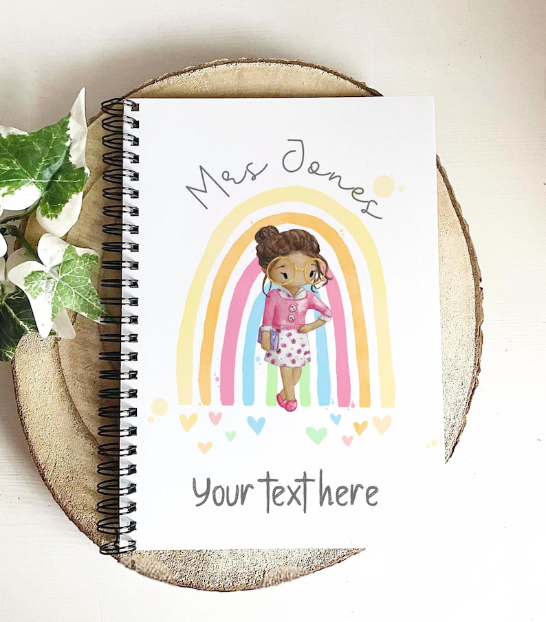 May include: Spiral-bound notebook with a colorful illustration of a person in front of a rainbow. The notebook cover has the text "Mrs Jones" and "Your text here". The person in the illustration is wearing glasses and a pink outfit.