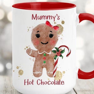 May include: White ceramic mug with a red interior and handle. The mug features a gingerbread person illustration with a red bow, holding a candy cane. The text "Mummy's Hot Chocolate" is printed on the mug.
