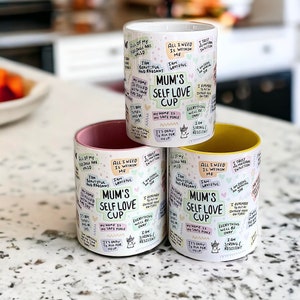May include: Three ceramic mugs with a white background and colorful text. The mugs have a pink, white, and yellow rim. The text on the mugs reads "Mum's Self Love Cup" and includes affirmations such as "All of my feelings are valid", "I am beautiful and radiant", "My home is filled with love", "It's okay to ask for help", "I trust my intuition", "I remember to put my oxygen mask on first", "Everything will be okay", "I am strong and resilient".