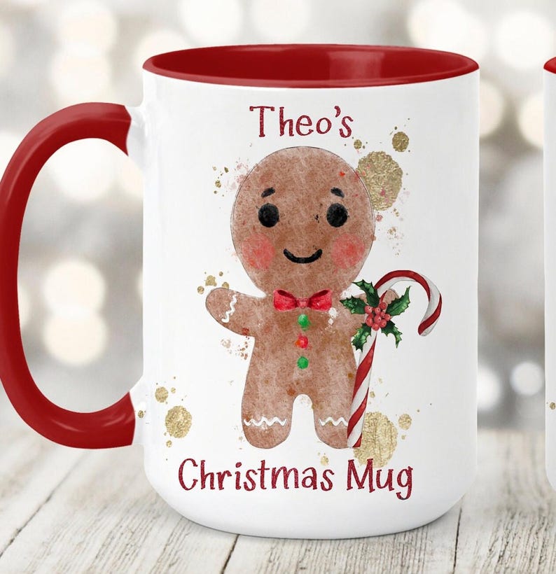 May include: White ceramic Christmas mug with a red handle and interior. The mug features a gingerbread man illustration with a candy cane and the text "Theo's Christmas Mug". Gold paint splatters are in the background.