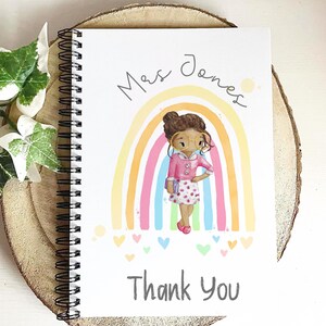 May include: Spiral-bound notebook with a colorful illustration. The cover features a cartoon of a teacher in front of a rainbow, with the words "Mrs. Jones" and "Thank You". The design includes hearts and a soft color palette.
