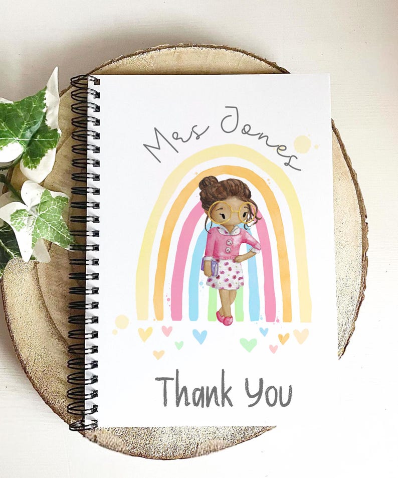 May include: Spiral-bound notebook with a colorful illustration. The cover features a cartoon of a teacher in front of a rainbow, with the words "Mrs. Jones" and "Thank You". The design includes hearts and a soft color palette.