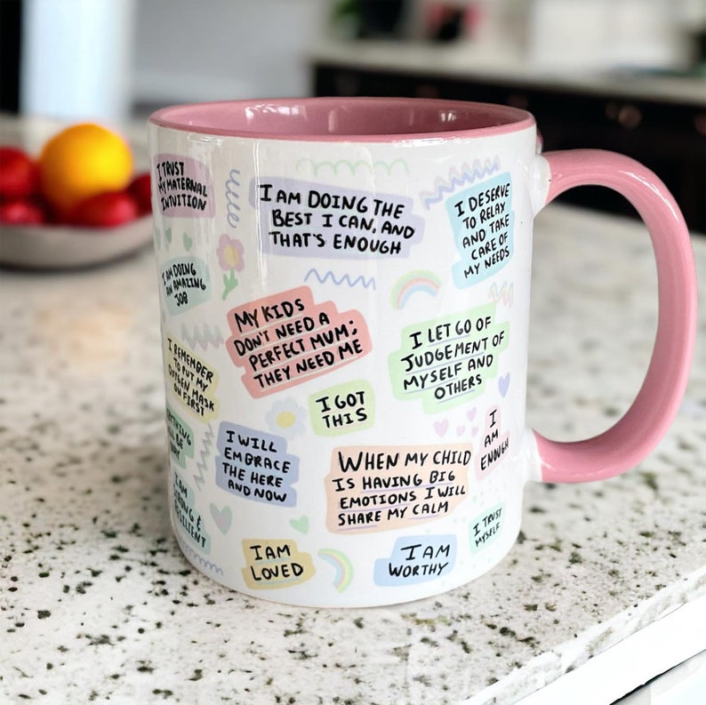 May include: White ceramic mug with a pink rim and handle. The mug is covered in colorful, handwritten affirmations, including "I am doing the best I can, and that's enough", "My kids don't need a perfect mum: they need me", "I got this", "I am loved", "I am worthy", and "When my child is having big emotions I will share my calm".