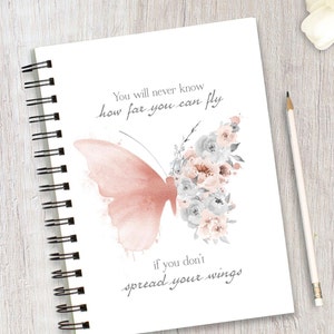 May include: A white notebook with a spiral binding features a watercolor illustration of a pink butterfly with gray and pink flowers. The notebook has the text "You will never know how far you can fly if you don't spread your wings".