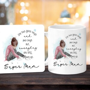 Peut inclure: Mug et dessous de verre blancs avec une illustration &agrave; l'aquarelle d'une personne assise, la t&ecirc;te baiss&eacute;e. Le texte dit : &laquo; She has good days and bad days but, everyday she still shows up. Super Mum. &raquo;