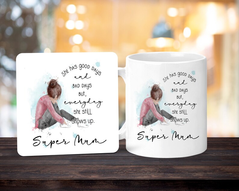Peut inclure: Mug et dessous de verre blancs avec une illustration &agrave; l'aquarelle d'une personne assise, la t&ecirc;te baiss&eacute;e. Le texte dit : &laquo; She has good days and bad days but, everyday she still shows up. Super Mum. &raquo;