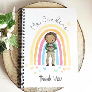 May include: White spiral-bound notebook with a colorful rainbow design and the words "Mr. Jenkins" and "Thank You." The illustration features a cartoon figure of a person standing in front of the rainbow. Small hearts are scattered at the bottom.