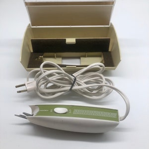 Könnte beinhalten: Vintage elektrische Haarschneidemaschine in Weiß und Grün mit weißem Kabel und beigefarbener Tragetasche. Der Trimmer hat einen grünen Streifen mit dem Text "Sears" und einen Schalter mit der Aufschrift "HI" und "LO". Die Tasche ist geöffnet und zeigt einen braunen Innenraum.
