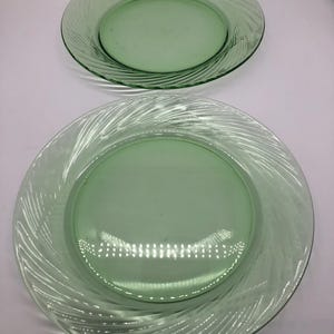 May include: Two green glass plates. The plates have a clear, swirled design around the edges. The plates are different sizes, with the smaller plate on top. The plates are a light green colour.