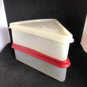 May include: A set of two triangular food storage containers. The top container has a translucent white base and a cream-colored lid. The bottom container is gray with a red rim. The containers are stacked on top of each other.