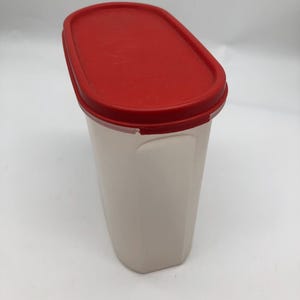 以下が含まれることがあります： 赤色の蓋が付いた、長方形のオフホワイトの容器。 蓋は楕円形で、ぴったりと上に収まります。 容器は、わずかにテクスチャ加工された表面を持っています。 ストレージ用に設計されています。