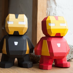 Puede incluir: Dos figuras de papel de Iron Man, una en negro y rojo y la otra en rojo y amarillo. Ambas figuras tienen una máscara facial amarilla con ojos blancos.
