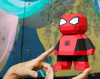 May include: A red and black papercraft figure of Spider-Man, standing on a person's hand. The figure has a black spider symbol on its chest.