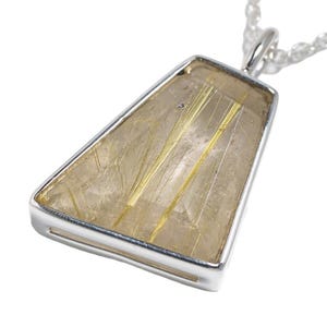 Pode incluir: Colar com pingente de prata com um pingente retangular contendo uma pedra clara marrom-claro. A pedra tem inclusões douradas em forma de agulha. O pingente é suspenso por uma delicada corrente de prata.