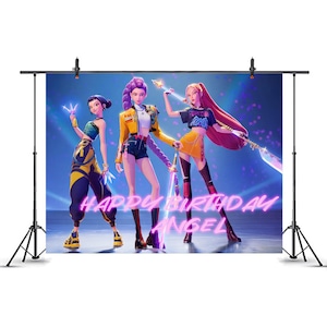 May include: A backdrop featuring three animated female figures in fashionable outfits, set against a blue background with glowing effects. The words "HAPPY BIRTHDAY ANGEL" are written in neon pink. The backdrop is supported by a black stand.