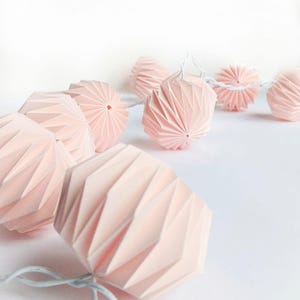 Può includere: Una ghirlanda di lanterne di carta rosa con filo bianco, perfetta per aggiungere un tocco di fantasia a qualsiasi spazio.