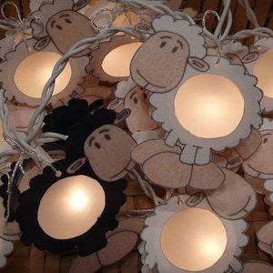 Könnte beinhalten: Eine Lichterkette aus weißen und schwarzen Schaf-förmigen Lichtern mit Glühbirnen im Inneren. Die Lichter sind mit einem weißen Kabel miteinander verbunden und hängen in einem Korb.