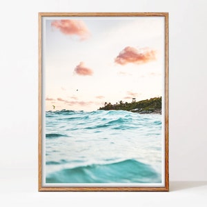 May include: A framed photograph of a turquoise ocean with waves crashing against the shore. The sky is a soft pink with fluffy clouds. A small island with trees and a building is visible in the distance.