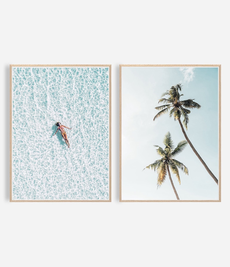 May include: Two framed art prints. One shows a person floating in turquoise water, the other depicts two tall palm trees against a light blue sky. Both prints are in light wood frames.