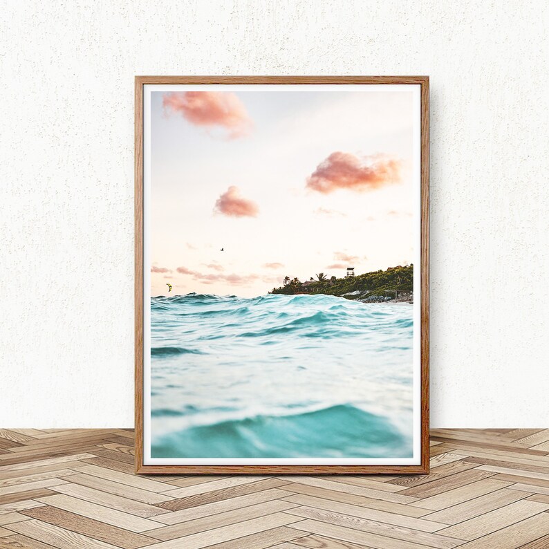 May include: A framed photograph of a turquoise ocean with waves crashing against the shore. The sky is a soft pink with fluffy clouds. A small island with trees and buildings is visible in the distance.