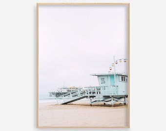 May include: A light blue lifeguard stand with a white wooden ramp leading to the beach. The stand has a number "13" on the side and a sign that reads "Lifeguard Station 13". The stand is on a sandy beach with a pier in the background.